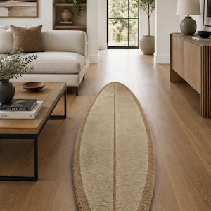 Puede incluir: Una alfombra alargada con forma de tabla de surf que presenta un panel central texturizado en color beige claro, bordeado por un ribete de textura peluda en tono bronceado oscuro. Una línea vertical recorre el centro de la alfombra.