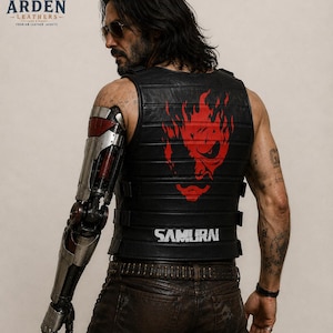 May include: A black leather vest featuring horizontal stitched panels, side buckle straps, and a prominent red graphic of a stylized face on the back. The word SAMURAI is printed in white lettering at the base of the vest, which is worn over dark pants.