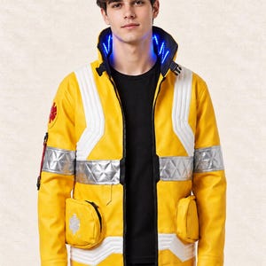 Pode incluir: Um casaco amarelo brilhante com painéis acolchoados brancos, faixas refletoras prateadas e uma gola alta com luzes LED azuis integradas. O casaco inclui dois bolsos frontais, um emblema médico vermelho na manga e um emblema prateado de estrela.