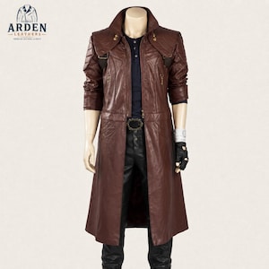 Puede incluir: Una gabardina larga de cuero marrón oscuro con cuello alto, botones dorados en los hombros y bolsillos con cremallera. El abrigo se lleva sobre una camisa azul oscuro y pantalones negros, con un guante negro sin dedos en una mano.