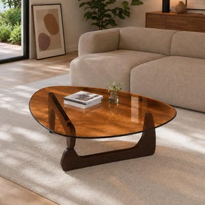 May include: A coffee table featuring a transparent, amber-tinted, organic-shaped glass top supported by a dark brown wooden base with two intersecting, curved structural elements that provide a stable foundation for the tabletop surface.