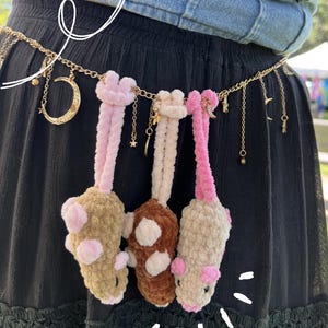 Könnte beinhalten: Ein goldfarbener Kettengürtel mit baumelnden Anhängern in Form von Mondsicheln und Sternen sowie drei plüschigen, gehäkelten Tierfiguren in Beige, Braun und Rosa. Der Text cottonandcandy ist am unteren Rand zu sehen.
