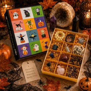 May include: A Halloween-themed gift box featuring a grid of cartoon characters on the lid and a divided tray containing various crystals, a small black padlock, a glass vial, a key-shaped charm, and an apple-shaped stone pendant.
