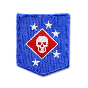 May include: A rectangular blue embroidered patch with a pointed bottom edge. The center features a red diamond containing a white skull. Five white stars are arranged in a curved pattern around the diamond on the blue background.