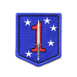 May include: A shield-shaped embroidered patch with a blue background and a black border. The design features a large red numeral one, a silver-colored vertical dagger superimposed over the numeral, and five white stars arranged around the center.
