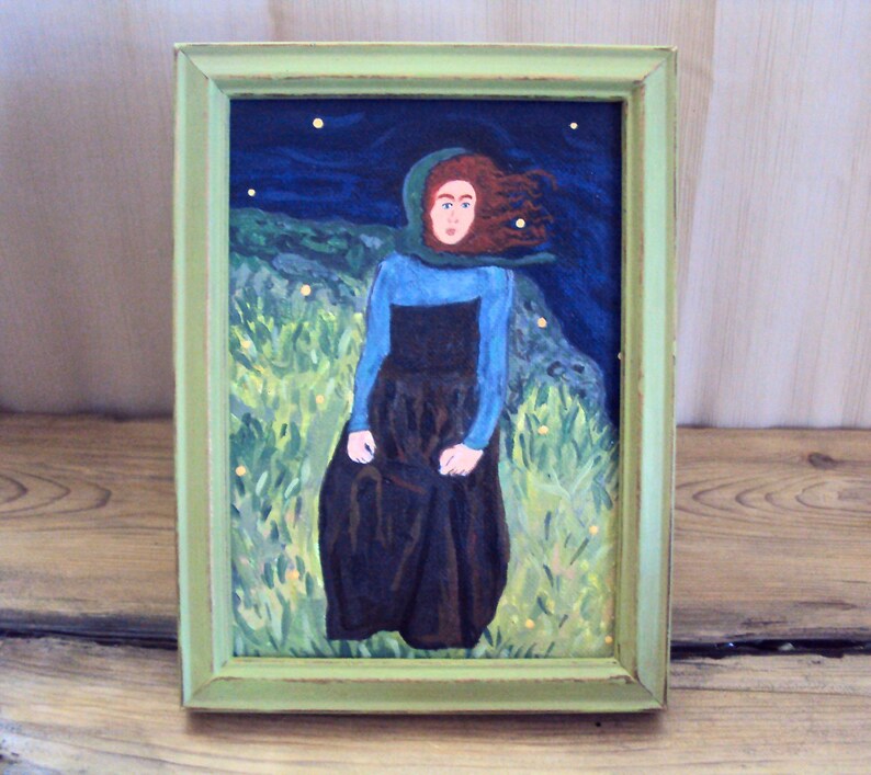 Op de afbeelding: Een ingelijst schilderij van een vrouw met rood haar die een blauwe en groene jurk draagt en in een veld met groen gras en gele bloemen staat. De achtergrond is een donkerblauwe lucht met witte sterren.