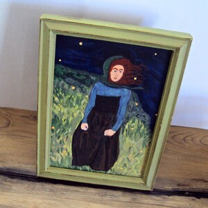 Op de afbeelding: Een ingelijst schilderij van een vrouw met rood haar die een blauwe en zwarte jurk draagt, staand in een veld met groen gras onder een donkerblauwe lucht met gele sterren.