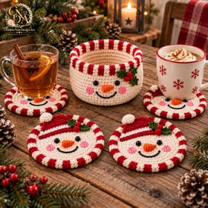 Puede incluir: Un juego de cuatro posavasos redondos de ganchillo y una cesta a juego, todos con un diseño de cara de muñeco de nieve con borde a rayas rojas y blancas, nariz de zanahoria, ojos negros y un pequeño detalle de acebo verde con bayas.