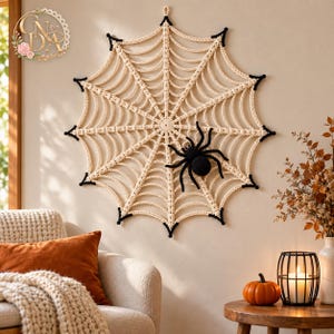 May include: A large, circular, cream-colored crocheted spider web wall hanging featuring black accents at the outer points. A black crocheted spider is attached to the lower right section of the web. The piece includes a small loop at the top for hanging.