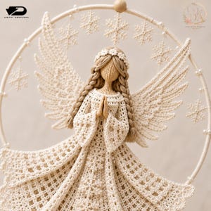 Puede incluir: Una figura de &aacute;ngel tejida a ganchillo de color crema con cabello trenzado y una diadema floral, con grandes alas y un vestido adornado con patrones de copos de nieve. El &aacute;ngel est&aacute; suspendido dentro de un aro circular decorado con perlas y copos.