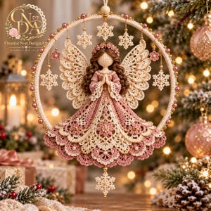 May include: A crocheted angel ornament suspended within a circular hoop adorned with pink beads and cream-colored snowflake motifs. The angel features brown hair, a pink dress with intricate lace detailing, and large, detailed cream-colored wings.