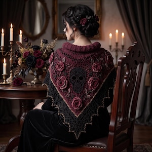 May include: A triangular crochet shawl featuring a deep burgundy and black color palette. The design includes a central black skull motif surrounded by three-dimensional dark red roses and intricate leaf patterns, finished with a pointed lace edge.