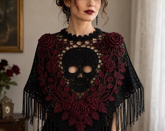 Puede incluir: Un chal de ganchillo negro con un motivo central de calavera rodeado de rosas y enredaderas de ganchillo en color burdeos oscuro. La prenda tiene un escote festoneado y largos flecos delicados en el borde inferior, creando un aspecto texturizado.