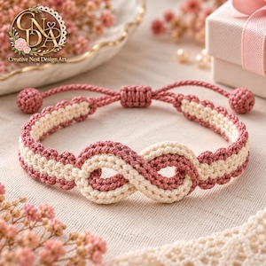 Puede incluir: Una pulsera de macramé con un diseño de símbolo de infinito hecho de cordones entrelazados en color rosa viejo y crema. La pulsera incluye un cierre deslizante ajustable con dos pequeños extremos anudados y un patrón trenzado texturizado.