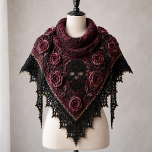 May include: A triangular crochet shawl featuring a deep burgundy and black color scheme. The design includes a central black skull motif surrounded by three-dimensional burgundy roses and intricate lace edges with subtle gold-toned accents.