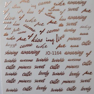 May include: A sheet of metallic copper-colored adhesive stickers featuring various words in cursive script, including love, kiss, princess, sweet, cute, twinkle, lovely, shining, and amaning, with the alphanumeric code JO-1164 printed in the center.