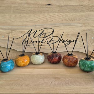 Puede incluir: Ocho difusores de varillas redondos hechos de madera pulida y resina de colores, cada uno con varillas negras. Los recipientes muestran patrones en espiral en verde, azul, amarillo, blanco, rojo y marrón. El texto MD Wood Design es visible al fondo.