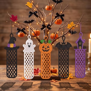 May include: Five hanging ornaments featuring Halloween motifs: a black witch hat, a white ghost, an orange jack-o'-lantern, a black bat, and a purple haunted house. Each ornament has a lattice-patterned base and a loop for hanging.