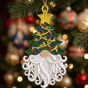 May include: A hanging Christmas ornament featuring an embroidered green pine tree topped with a yellow star. The tree is decorated with yellow string lights and multi-colored bulbs. Below the tree is a gnome with a tan nose and a white beard.