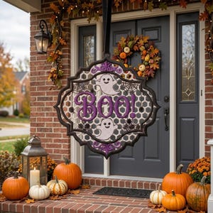 May include: A hanging decorative sign with a black frame and white honeycomb mesh center. The sign features purple embroidered text that reads BOO! along with two white ghost figures and black spider web accents, suspended by a black ribbon.