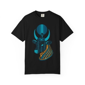 Puede incluir: Una camiseta negra de manga corta con un estampado gráfico de una cabeza de toro estilizada en tonos azules y dorados. El toro tiene un diseño de luna creciente y sol circular sobre su cabeza, con patrones intrincados en la cara y el cuello.