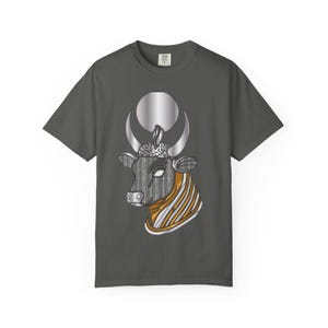 Puede incluir: Una camiseta gris carbón de manga corta con un gráfico de una cabeza de toro con un disco solar plateado y cuernos en forma de media luna. El toro tiene un patrón texturizado en blanco y negro en la cara y el cuello con detalles dorados y plateados.