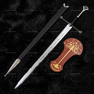 May include: A silver-toned metal sword with a black leather-wrapped grip and a crossguard. The blade features engraved runes and a star symbol. It is accompanied by a long black scabbard with a silver tip and a separate brown plaque with a gold tree design.