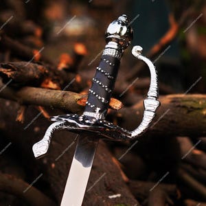 May include: A sword featuring a polished silver-tone metal hilt with a curved knuckle guard and a black grip wrapped in a silver-tone wire spiral. The pommel is rounded and metallic, leading to a straight, smooth, reflective steel blade.