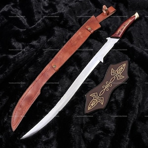 May include: A long, curved sword with a silver-toned blade, a dark reddish-brown wooden handle with gold-colored accents, a brown leather scabbard with metal studs, and a separate dark brown leather sheath piece featuring gold-colored leaf designs.