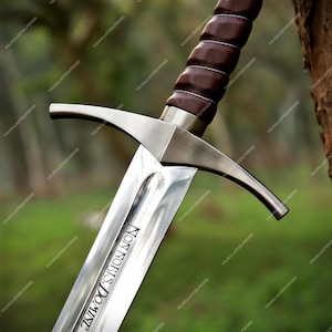 May include: A steel sword featuring a brown leather-wrapped grip with silver wire accents, a polished metal crossguard, and a blade engraved with the Latin text Non Nobis Domine. The blade has a central fuller running down its length.