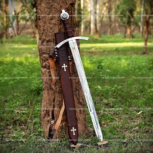 May include: A steel sword with a dark brown leather-wrapped hilt and a matching brown leather scabbard. The crossguard features the engraved text "CHRISTUS VINCIT" and a small cross. The scabbard is decorated with two white cross emblems.