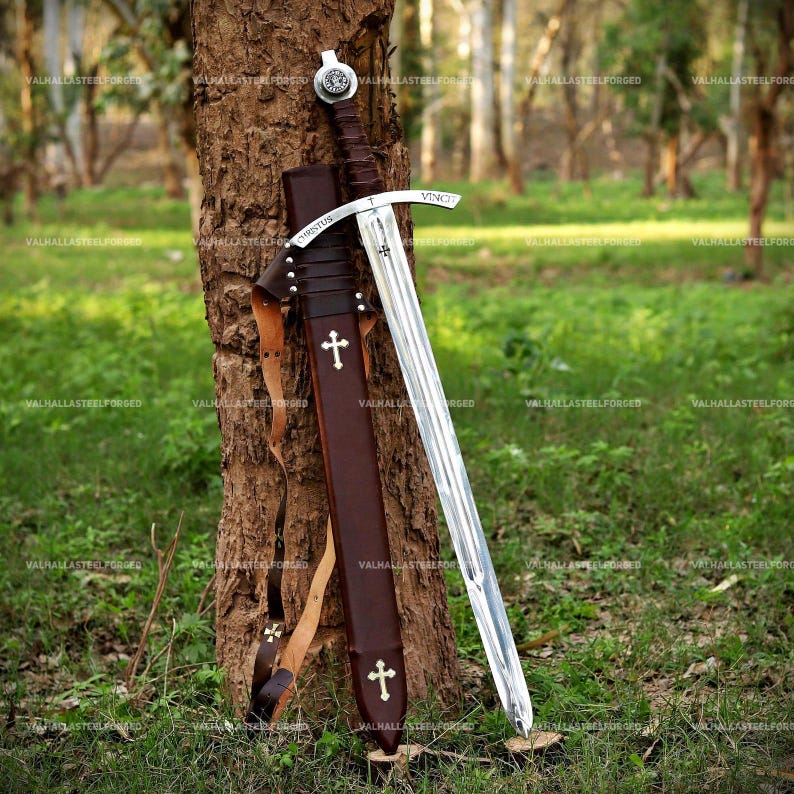 May include: A steel sword with a dark brown leather-wrapped hilt and a matching brown leather scabbard. The crossguard features the engraved text "CHRISTUS VINCIT" and a small cross. The scabbard is decorated with two white cross emblems.
