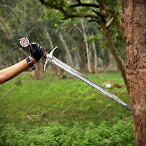 May include: A long steel sword with a double-edged blade and a crossguard. The pommel features a circular emblem with a red cross. The blade is engraved with text and is pointed into the side of a tree trunk. The hilt is wrapped in dark material.