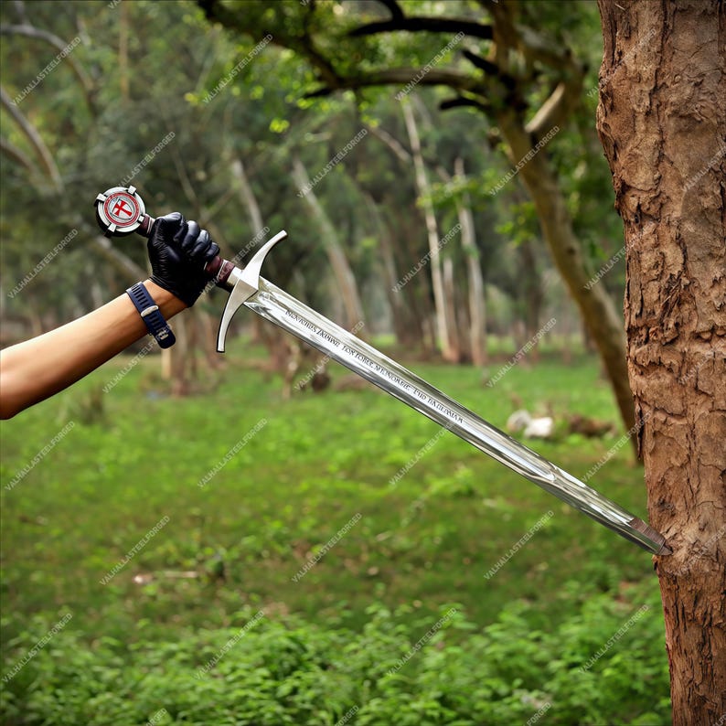 May include: A long steel sword with a double-edged blade and a crossguard. The pommel features a circular emblem with a red cross. The blade is engraved with text and is pointed into the side of a tree trunk. The hilt is wrapped in dark material.