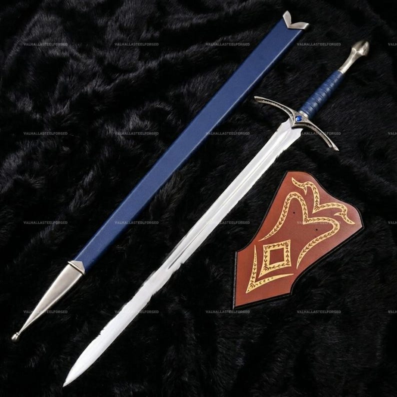 May include: A silver metal sword with a blue leather-wrapped handle, a blue scabbard with silver metal accents, and a brown leather wall plaque featuring gold-colored decorative patterns. The sword crossguard includes a small blue gemstone.