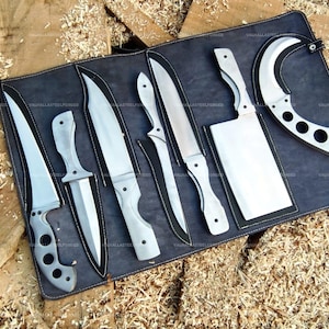 Puede incluir: Un juego de seis cuchillos de metal plateado y un cuchillo de carnicero dispuestos sobre un rollo de cuero gris oscuro. La colección incluye varias formas de hoja, incluida una hoja curva tipo karambit con recortes circulares y un cuchillo grande.