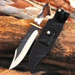 Puede incluir: Un cuchillo de hoja fija con una hoja de acero forjado oscuro, una guarda de latón y un mango de asta marrón texturizado. El cuchillo viene acompañado de una funda de cuero negro que cuenta con un pequeño bolsillo frontal con un broche metálico.