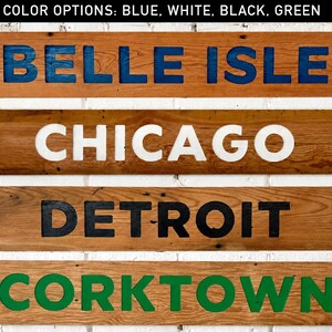 K&ouml;nnte beinhalten: Vier rechteckige Holzschilder mit vertiefter Beschriftung. Das oberste Schild zeigt BELLE ISLE in Blau, das zweite CHICAGO in Wei&szlig;, das dritte DETROIT in Schwarz und das untere Schild CORKTOWN in Gr&uuml;n. Der Text oben lautet COLOR OPTIONS: BLUE, WHITE, BLACK, GREEN.