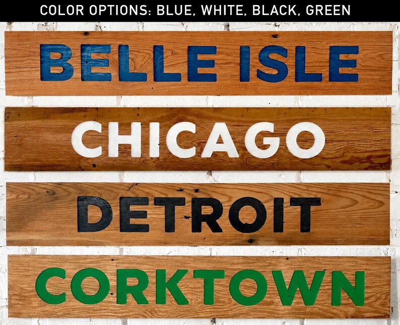 K&ouml;nnte beinhalten: Vier rechteckige Holzschilder mit vertiefter Beschriftung. Das oberste Schild zeigt BELLE ISLE in Blau, das zweite CHICAGO in Wei&szlig;, das dritte DETROIT in Schwarz und das untere Schild CORKTOWN in Gr&uuml;n. Der Text oben lautet COLOR OPTIONS: BLUE, WHITE, BLACK, GREEN.