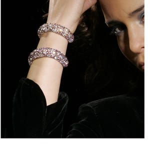 Peut inclure: Deux bracelets assortis présentant une surface dense et arrondie recouverte de petits cristaux réfléchissant la lumière. Les cristaux présentent une teinte rose pâle irisée et argentée, créant un effet scintillant sur la structure tubulaire.