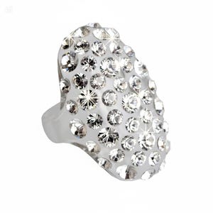 May include: A clear ring featuring a large, oval-shaped face completely covered in numerous, sparkling, clear crystals. The band is a simple, clear design. The ring's design is intended to be a bold statement piece, with the crystals catching the light.