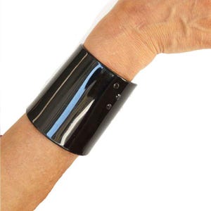 Könnte beinhalten: Ein schwarzes Keramik-Armband mit zwei dünnen goldenen Linien und kleinen Löchern an der Seite.
