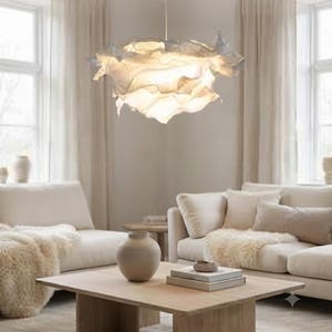 May include: A white pendant light fitting with a layered, ruffled, cloud-like shade suspended from the ceiling. The light emits a soft, warm glow from within the translucent, overlapping material, creating a textured and voluminous appearance.