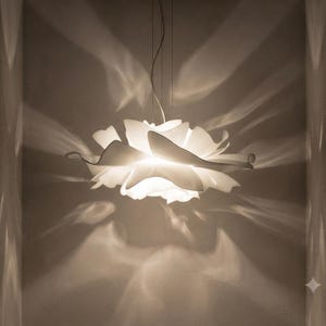 Può includere: Una lampada a sospensione bianca con molteplici strati sovrapposti, curvi e a forma di petalo che emettono una luce morbida e calda. La luce proietta ombre distinte, allungate e ondulate sulle pareti circostanti, creando un effetto luminoso.