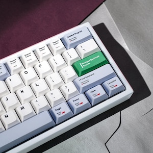May include: A mechanical keyboard featuring white keycaps with black lettering and light blue accent keys. Specific keys are labeled with text including Laplace Program, Newtype-Destroyer System, I-Field Generator, Launcher, Hyper, Frame, and Toggle.