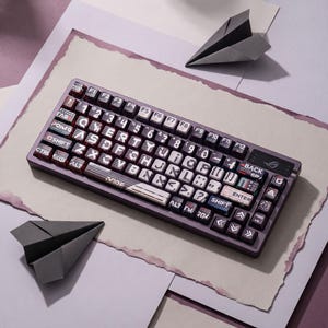 May include: A dark purple mechanical keyboard featuring custom keycaps with white graphic lettering, symbols, and the text "ENTER", "BACK SP", "SHIFT", and "ROG" logo. The keyboard has a compact layout with function keys and arrow keys.