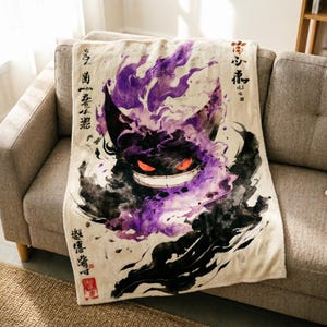 Puede incluir: Una manta de color crema con una ilustración estilo acuarela de una criatura morada y negra con ojos rojos brillantes y una amplia sonrisa. El diseño incluye caligrafía japonesa en negro y un sello cuadrado de color rojo en la esquina.