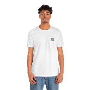 Op de afbeelding: Een wit T-shirt met korte mouwen en een ronde hals, voorzien van een kleine, vierkante zwart-witte grafische print op de linkerborst. Het shirt wordt gecombineerd met een blauwe spijkerbroek voor een eenvoudige en strakke dagelijkse uitstraling.