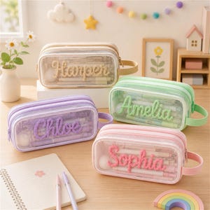Puede incluir: Cuatro estuches rectangulares con frente transparente y parte posterior de tela de color. Cada estuche presenta un nombre personalizado en hilo texturizado: Harper en beige, Amelia en verde claro, Chloe en morado y Sophia en rosa. Asa lateral.
