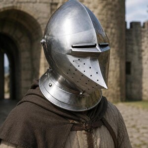 May include: A polished steel bascinet helmet with a pointed visor, narrow horizontal eye slits, and a series of small ventilation holes on the front. The helmet features a rounded dome and a flared neck guard, resting above a quilted beige tunic.